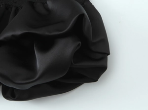 Detailed close-up of premium black satin fabric with elegant wave pleats and silky texture