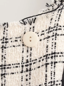 Close-up of black and white tweed fabric with fringe edge and cream round button