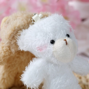 Close-up of a white plush teddy bear charm with pink blush and metal keychain ring