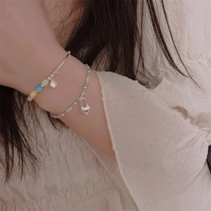 Detail of silver bangle with colorful beads and pearl heart charm on a woman's wrist