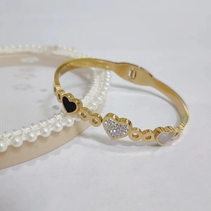 Detail of gold watchband bracelet featuring heart charms with enamel and mother of pearl