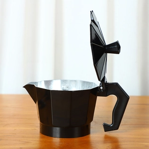 Detailed view of an open black aluminum moka pot on a wooden table with soft lighting