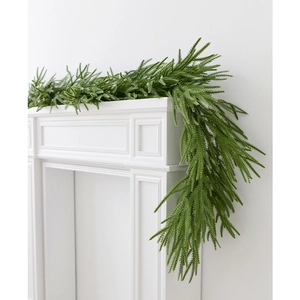 Realistic green PE Norfolk pine garland hanging on a modern white fireplace mantel