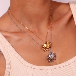 Primer plano de collares superpuestos con colgante de cangrejo en oro y plata en modelo