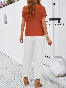 Detail view of orange knit short sleeve top and white cropped lantern pants on a model