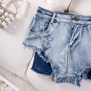 Dettaglio di pantaloncini di jeans azzurri con bordi sfrangiati e decorazioni di perle