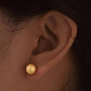 Close-up of a minimalist golden stainless steel ball earring with a matte finish