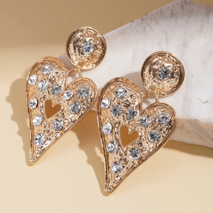 Gros plan sur des boucles d'oreilles cœur vintage dorées et cristaux sur marbre