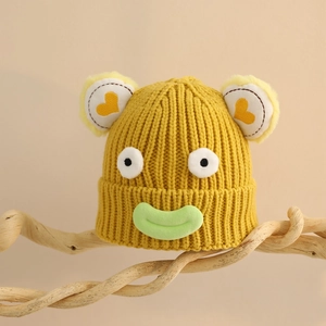 Détail d'un bonnet en maille jaune avec yeux de dessin animé et lèvres vertes sur branche