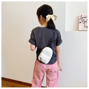 Kid model wearing a white nylon mini crossbody chest bag with adjustable black strap