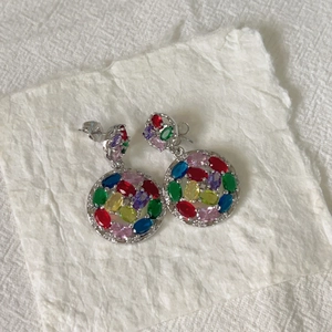 Close-up of double-layered round silver earrings with colorful zircon stones on white paper