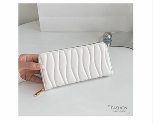 Detail of white long PU leather purse featuring wavy quilted pattern and gold zipper