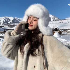 Detailed close-up of a white plush trapper hat worn with a wool coat in a snowy landscape