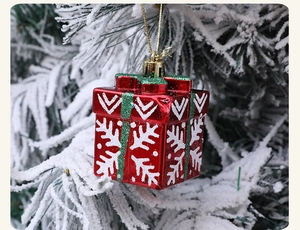 Close-up of red Christmas gift box ornament with green glitter on snowy pine branch