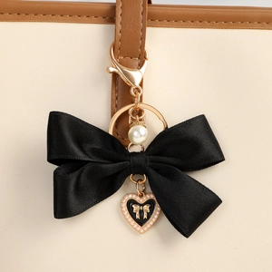 Detail of a black fabric bow keychain with heart pendant and pearl on a beige handbag