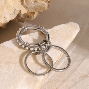 Three-layer stacked stainless steel ring set with white pearls on a stone background