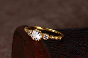 Macro shot of gold vintage three-stone ring with milgrain detailing and clear gems