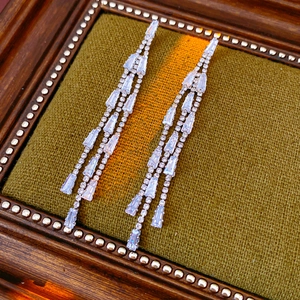 Detail of silver drop earrings with shimmering rectangular zirconia tassels on green velvet
