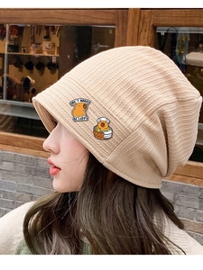 Détail du bonnet en tricot beige avec des pins Capybara et un badge de slogan mignon