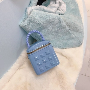 Close-up of light blue jelly bucket bag with pyramid studs and woven handle detail