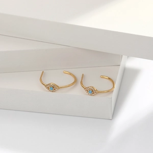 Detail of gold evil eye C-shaped hoop earrings with blue opal and white zircon stones