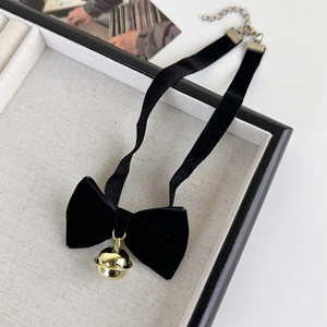 Détail d'un choker en velours noir avec nœud et pendentif clochette dorée sur tissu