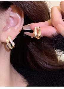 Macro detail of gold double-layered geometric earrings with white shell and zircons