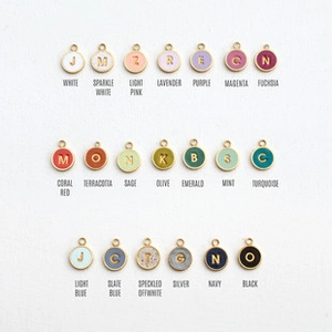 Vue à plat de pendentifs lettres colorés en émail avec bordure dorée sur fond blanc