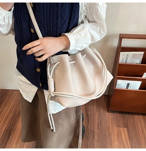 Detail view of cream drawstring bucket bag with litchi texture and decorative shoulder knot