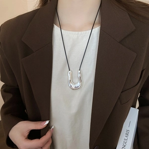 Close-up of polished silver U-shaped metal pendant on a minimalist black cord necklace