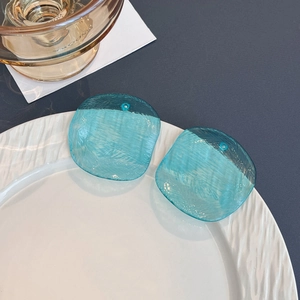Blue translucent acrylic earrings with ripple texture on a white ceramic plate