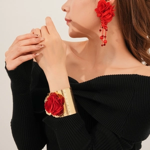 Détail de la boucle d'oreille fleur en tissu rouge avec pompons et bracelet doré