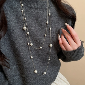 Close-up of double-layer pearl necklace on grey sweater with golden chain details
