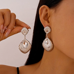 Close-up of textured silver shell-shaped earrings worn by a model for a summer beach look