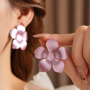 Vue détaillée de grandes boucles d'oreilles fleurs en métal rose mat portées