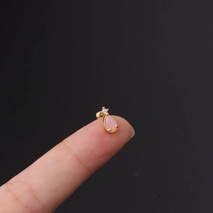 Macro view of tiny pink teardrop zircon stud earring with gold base on fingertip