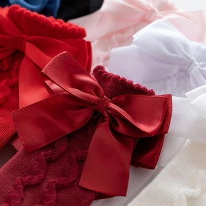 Close-up of cable knit baby socks featuring large bows in vibrant festive red colors