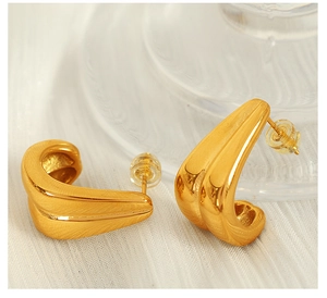 Detail of gold 18K plated C-shape earrings with a textured surface on white fabric