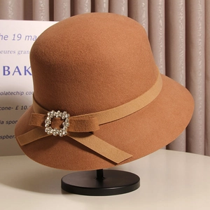 Vue détaillée du chapeau cloche en laine camel avec boucle en strass et nœud sur socle