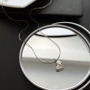 Elegant silver heart pendant necklace on mirror surface with sleek beaded metal chain link