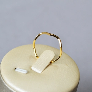 Detail of a wave-shaped gold-plated brass ring on a beige textured display stand