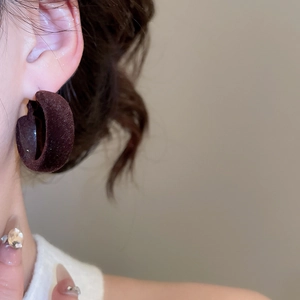 Gros plan de créoles en forme de C en velours marron foncé portées par un mannequin