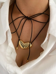 Detail of a minimalist gold heart pendant on a black cord worn with a white shirt