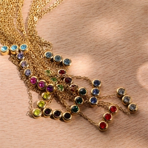 Collier pierres de naissance en acier doré avec zircons ronds sur fond bois naturel