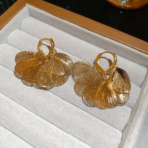 Close-up of gold hollow leaf earrings with textured veins on grey velvet jewelry box