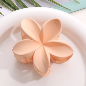 Détail d'une pince à cheveux fleur de frangipanier rose mat sur une assiette blanche