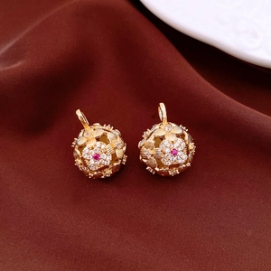 Macro view of gold spherical earrings with floral engravings and red gemstones