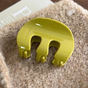 Close-up of a glossy yellow M-shaped acrylic hair claw clip on soft beige plush fabric