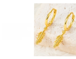 Close-up of S925 sterling silver gold feather hoop earrings on a stone texture background