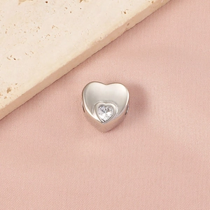 Polished silver heart bead with a sparkling zircon center on elegant pink silk background